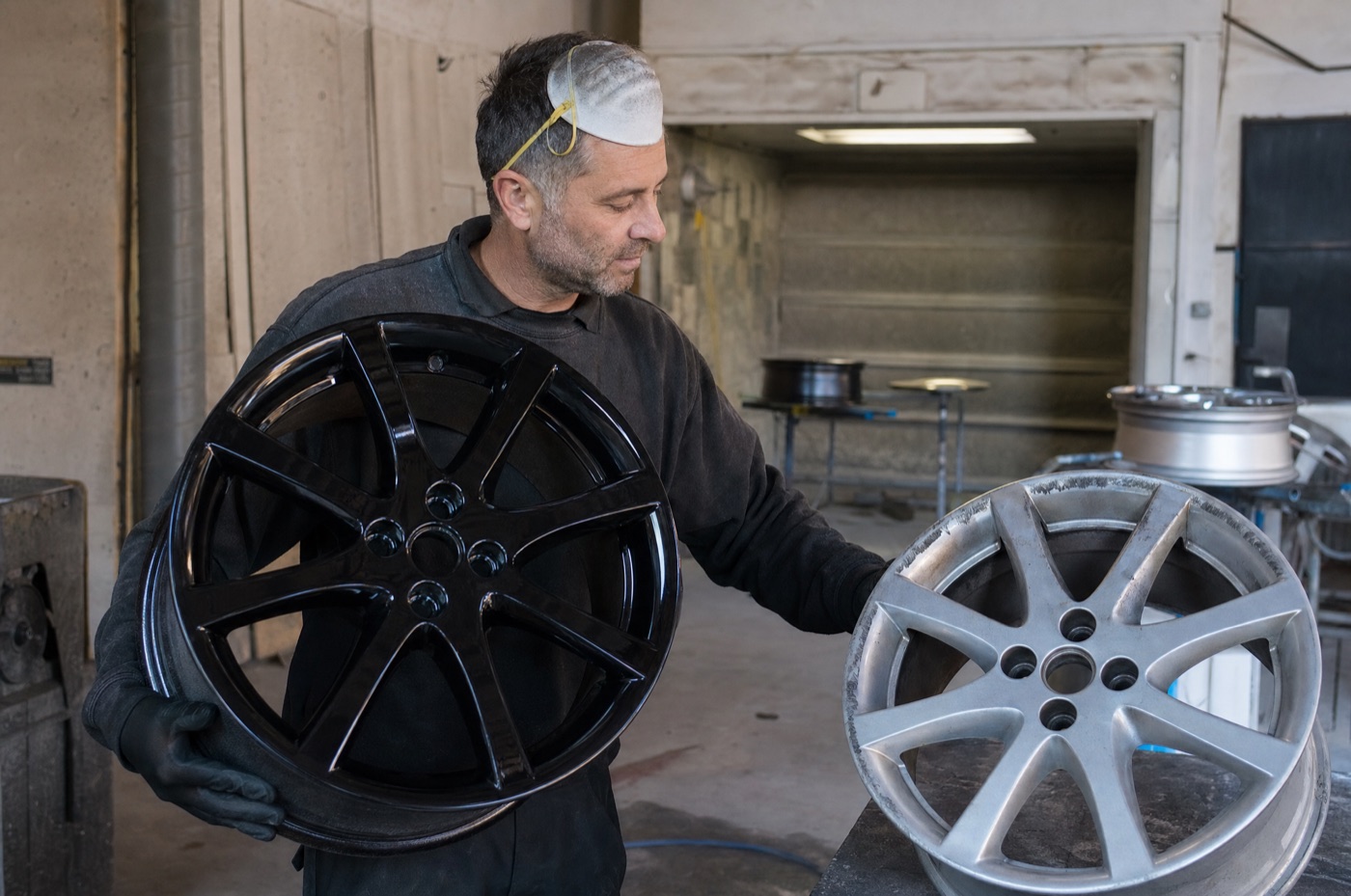 A detailer scrubbing the spokes of an alloy wheel with a long-handled brush